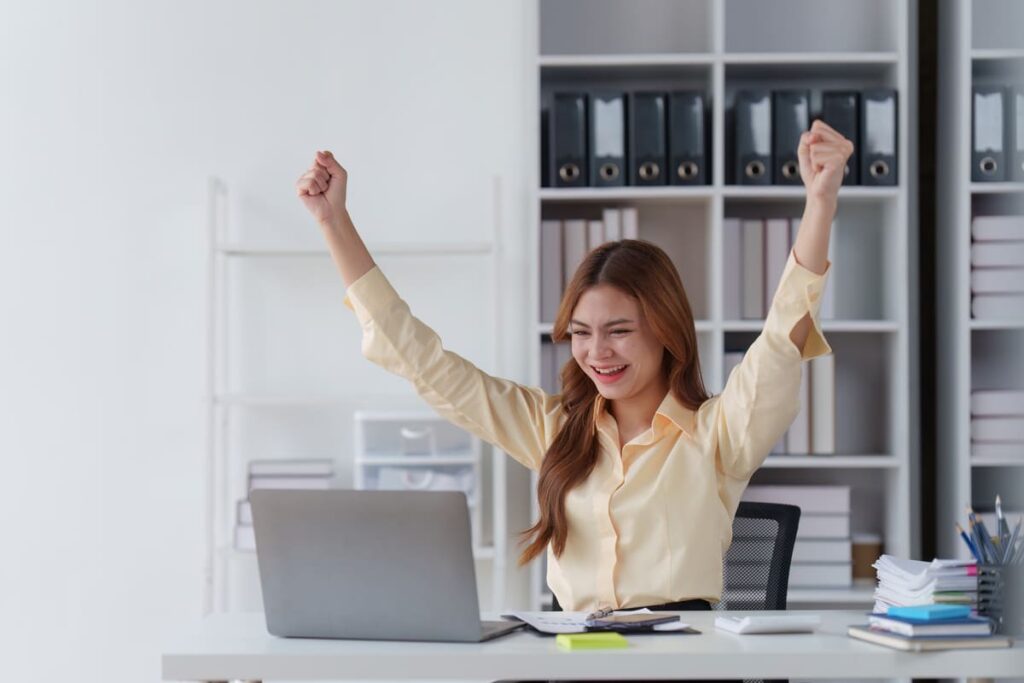 woman sitting at desk with arms up cheering